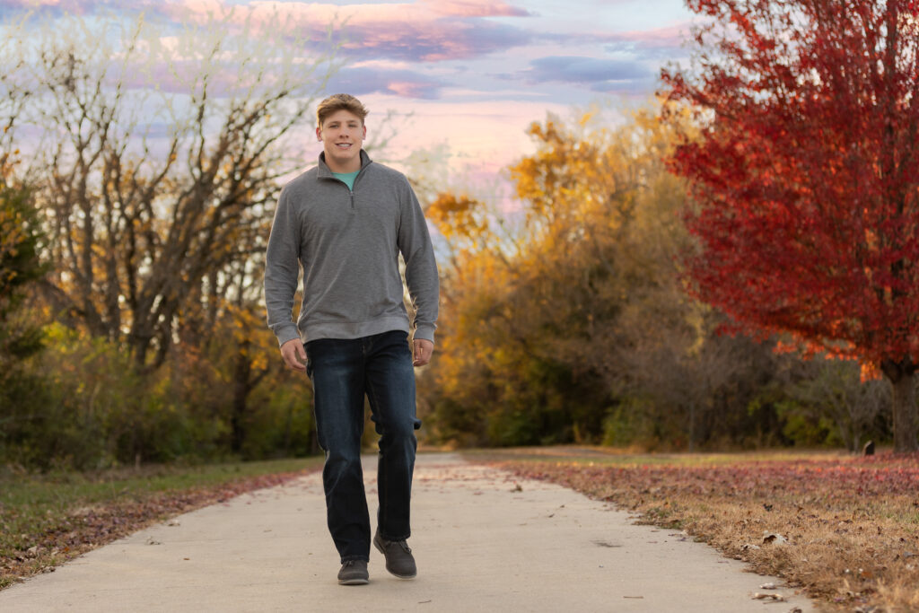 Senior guy during fall senior pictures session walking a tree-lined path at golden hour – Megan Bowers Photography