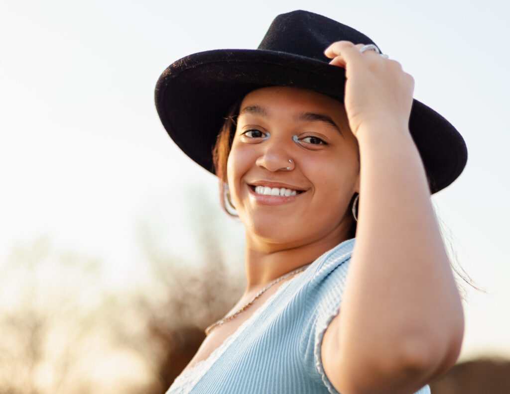 Teen girl smiling in soft blue dress and wide-brim hat at golden hour