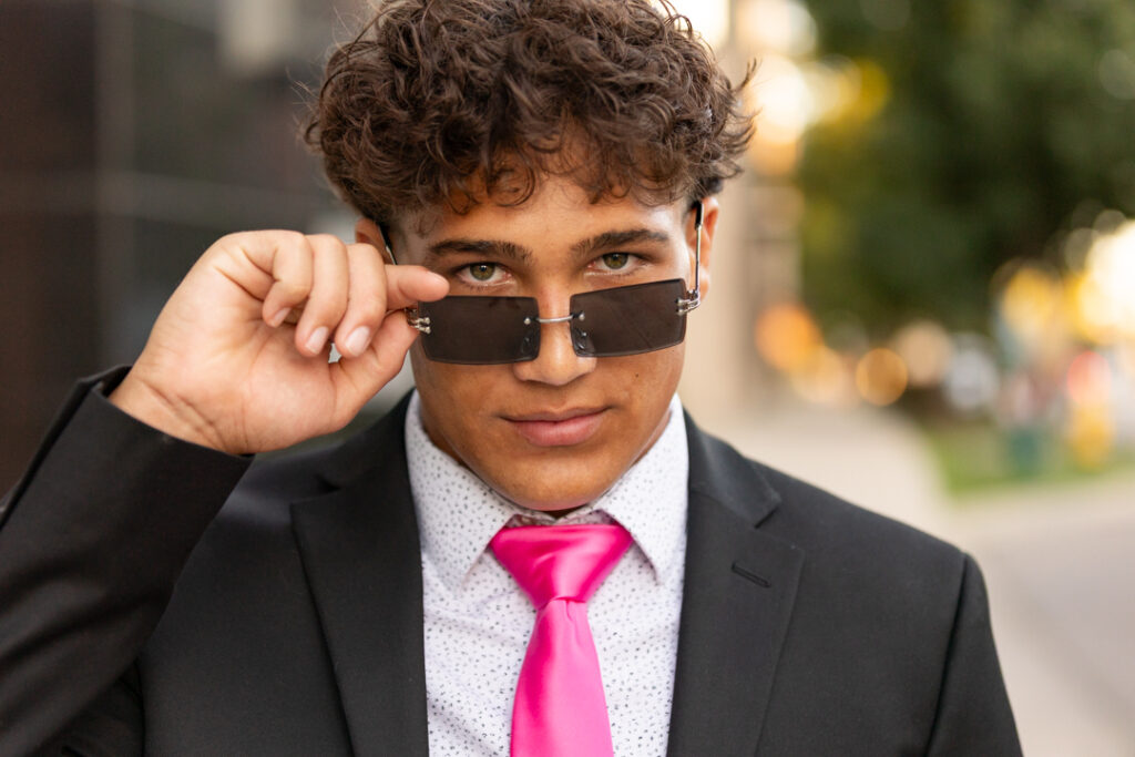 Teen guy wearing a black suit and pink tie during senior portrait shoot