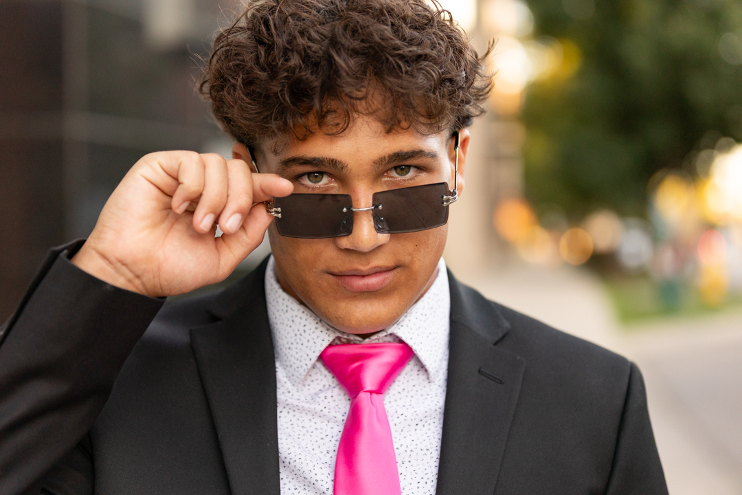 Teen guy wearing a black suit and pink tie during senior portrait shoot