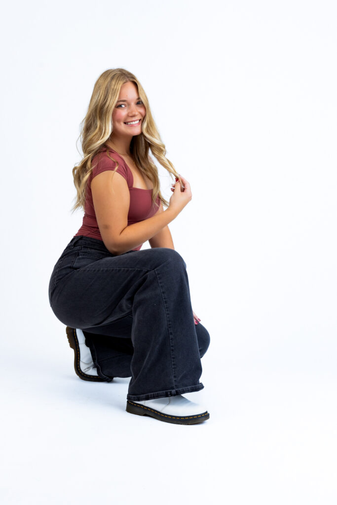 Senior girl in maroon top and black jeans during indoor photo session