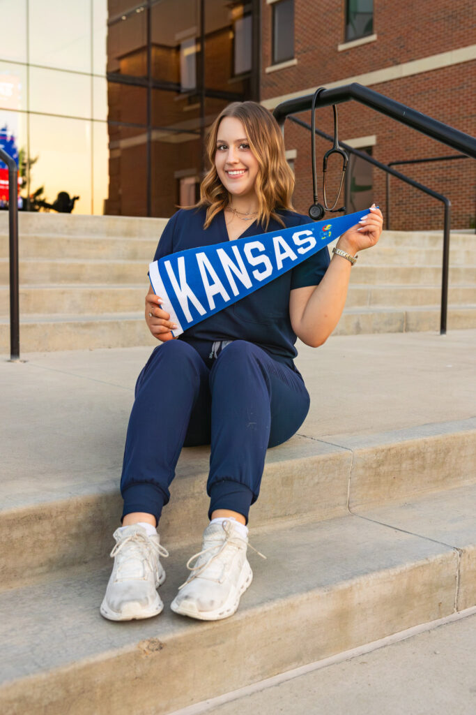 University of Kansas campus senior photos, Free State senior wearing blue nursing scrubs with stethoscope and KU pendant
