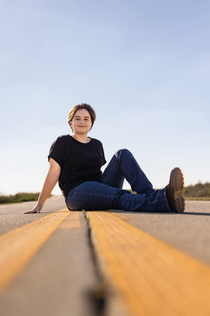 Amelia sitting on the road in a black shirt for an edgy senior portrait session in Lawrence, KS