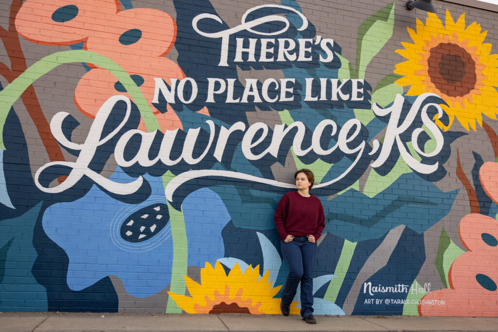 Amelia standing by the “There’s No Place Like Lawrence, KS” mural during downtown senior photos on Mass St