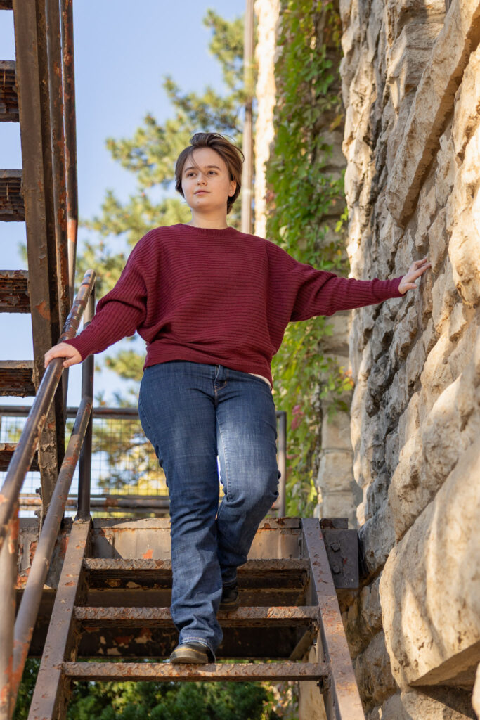 Amelia walking down metal stairs in a maroon sweater during senior portraits on the KU campus in Lawrence, KS
