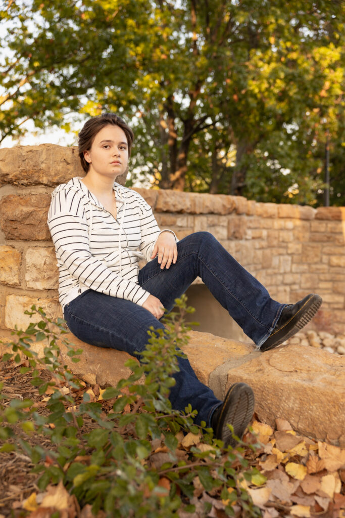 Amelia sitting on a stone wall during senior portraits on the KU campus in Lawrence, Kansas