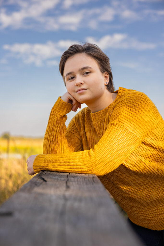 Close-up senior portrait of Amelia in a mustard sweater at Baker Wetlands in Lawrence, Kansas