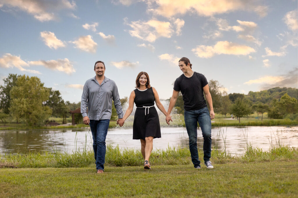 Family of three walking together laughing near a pond in Lawrence KS during a senior family photo session before graduation