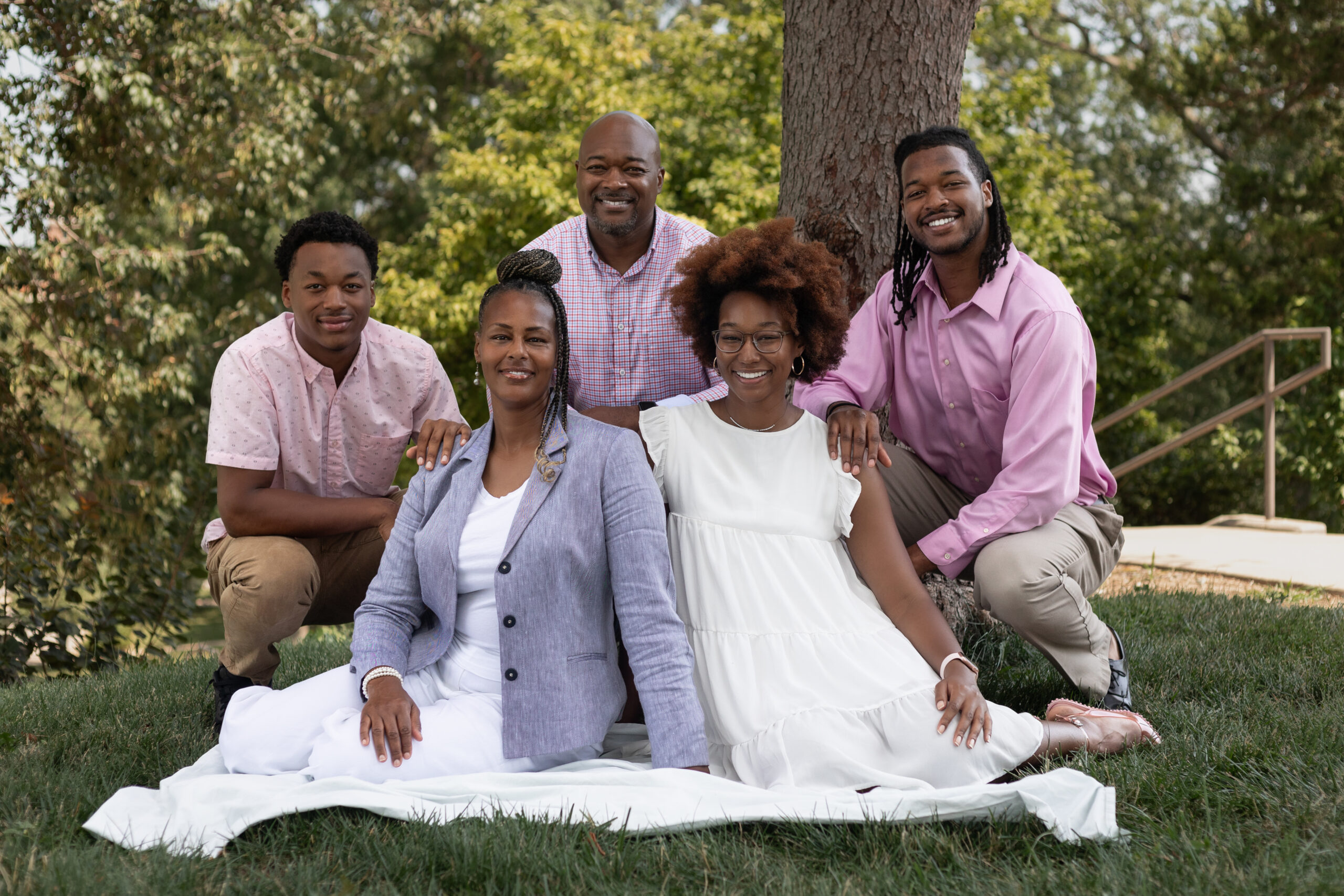 Family of five smiling together outdoors under a tree in Lawrence KS during a senior family photo session before graduation