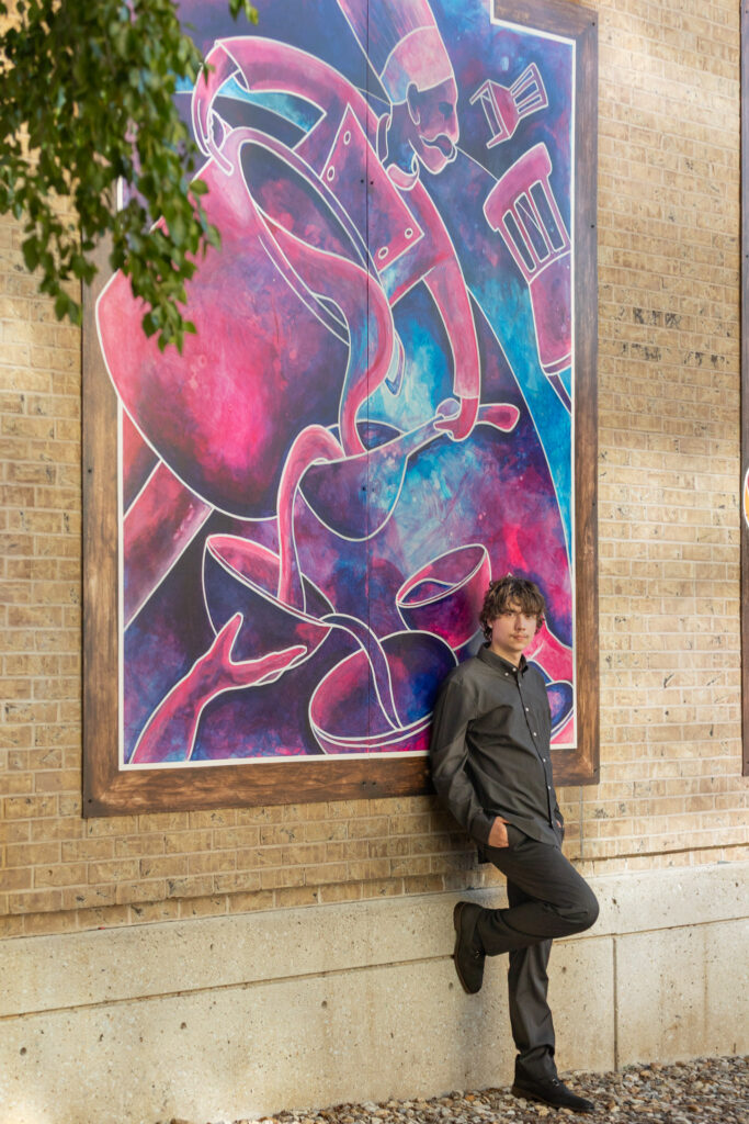 High school senior boy posing by a colorful mural on a brick wall in Lawrence