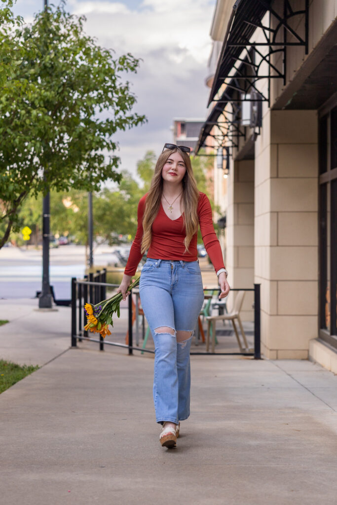 High school senior walking on Mass Street in downtown Lawrence holding sunflowers