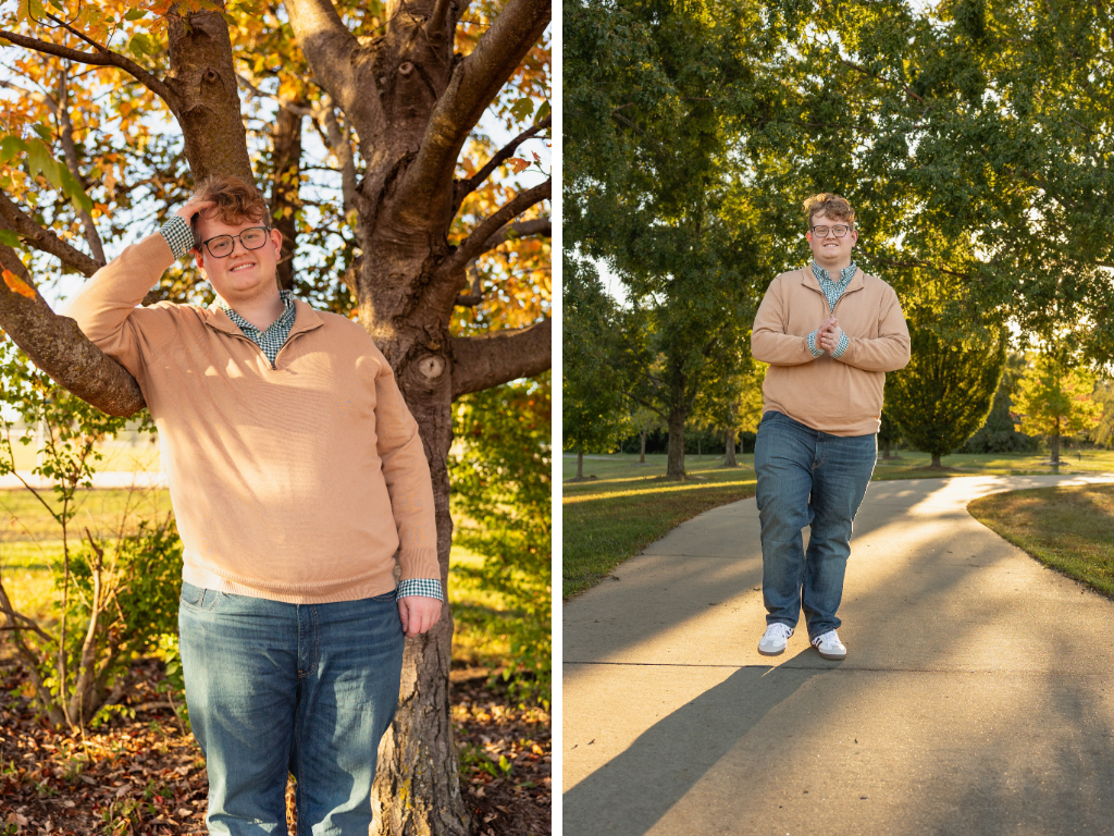 Senior in a tan quarter-zip and green checked shirt by a tree and a sunlit, tree-lined path at the Lawrence Arboretum in fall