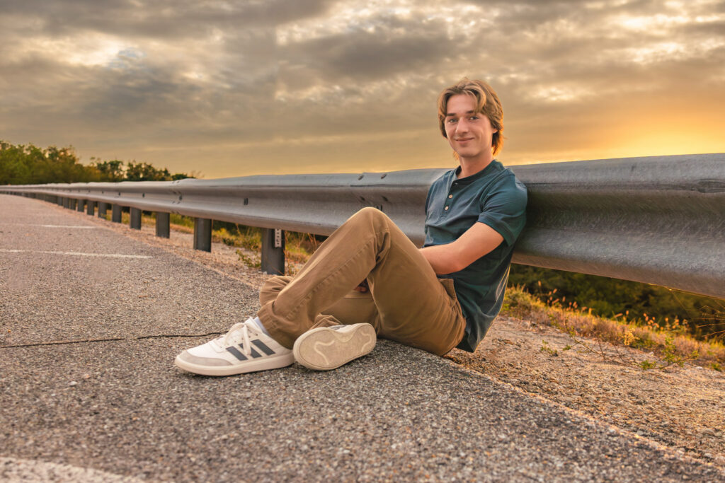 Senior boy sitting along a rural road at sunset during his Lawrence KS senior portrait session