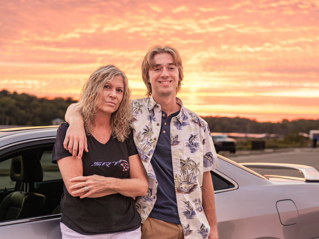 High school senior with his arm around his mom at sunset during his senior session.