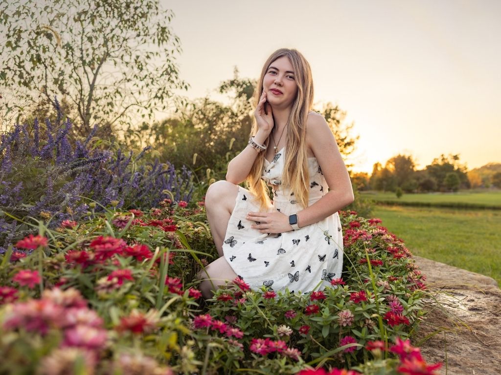 Lily in a white butterfly-print dress kneeling among pink and purple flowers at the Lawrence Arboretum at golden hour