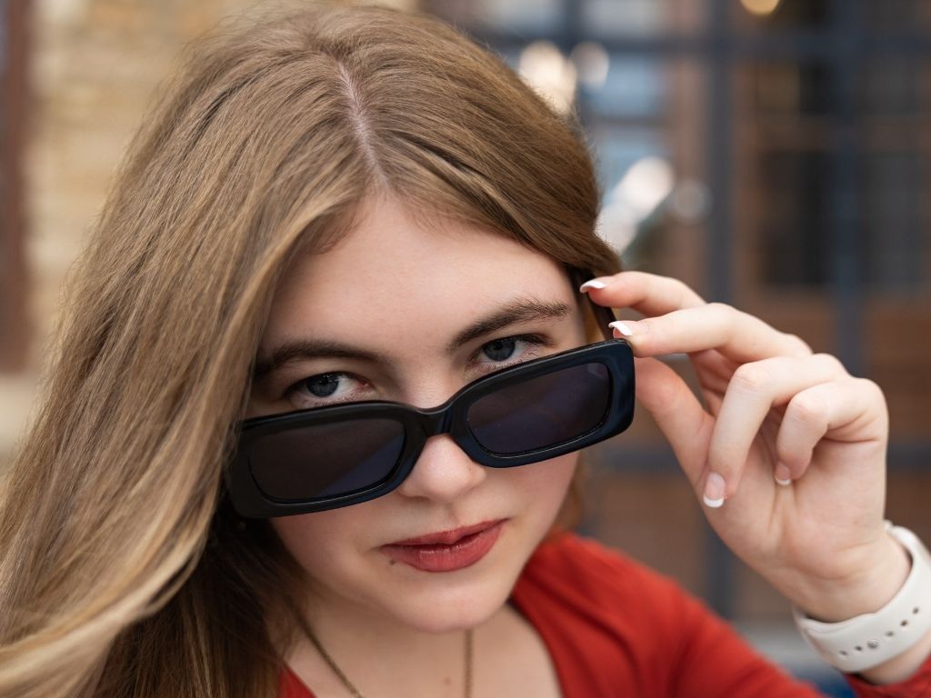 Topeka West senior pictures of Lily in a red top, lowering black sunglasses in Downtown Lawrence